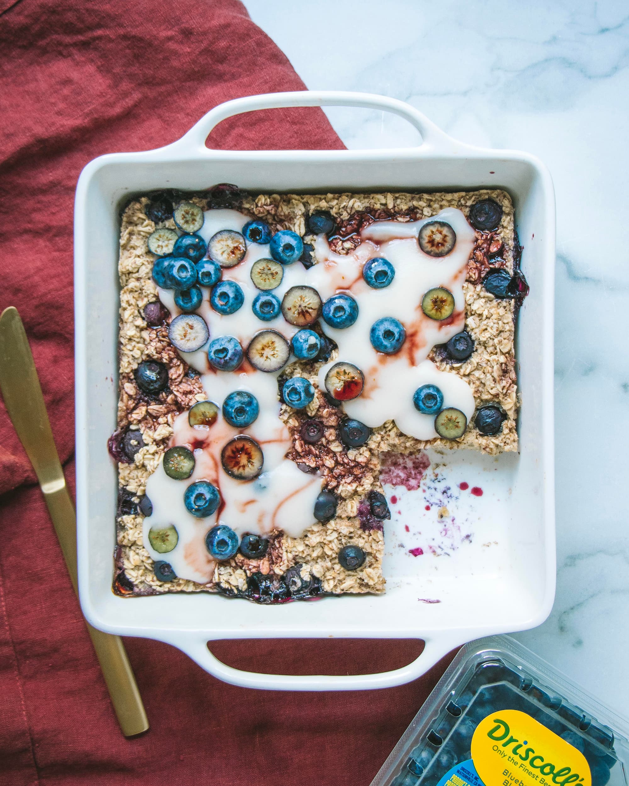 Blueberry baked oatmeal in a dish topped with a cream sauce and fresh blueberries