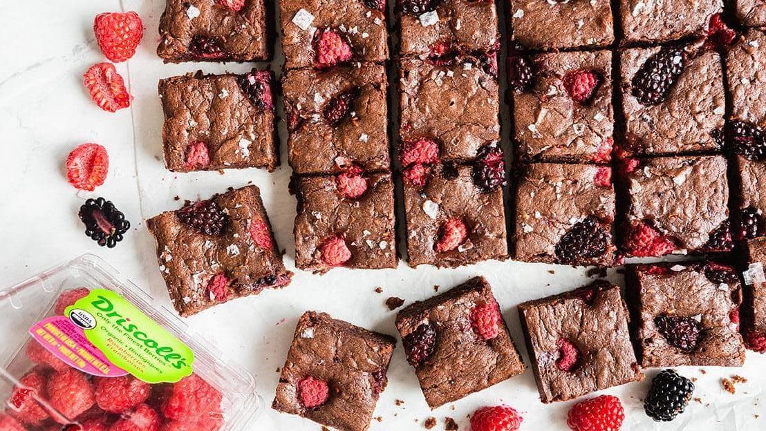 Brownie squares with raspberries and blackberries next to a clamshell of organic Driscoll's raspberries
