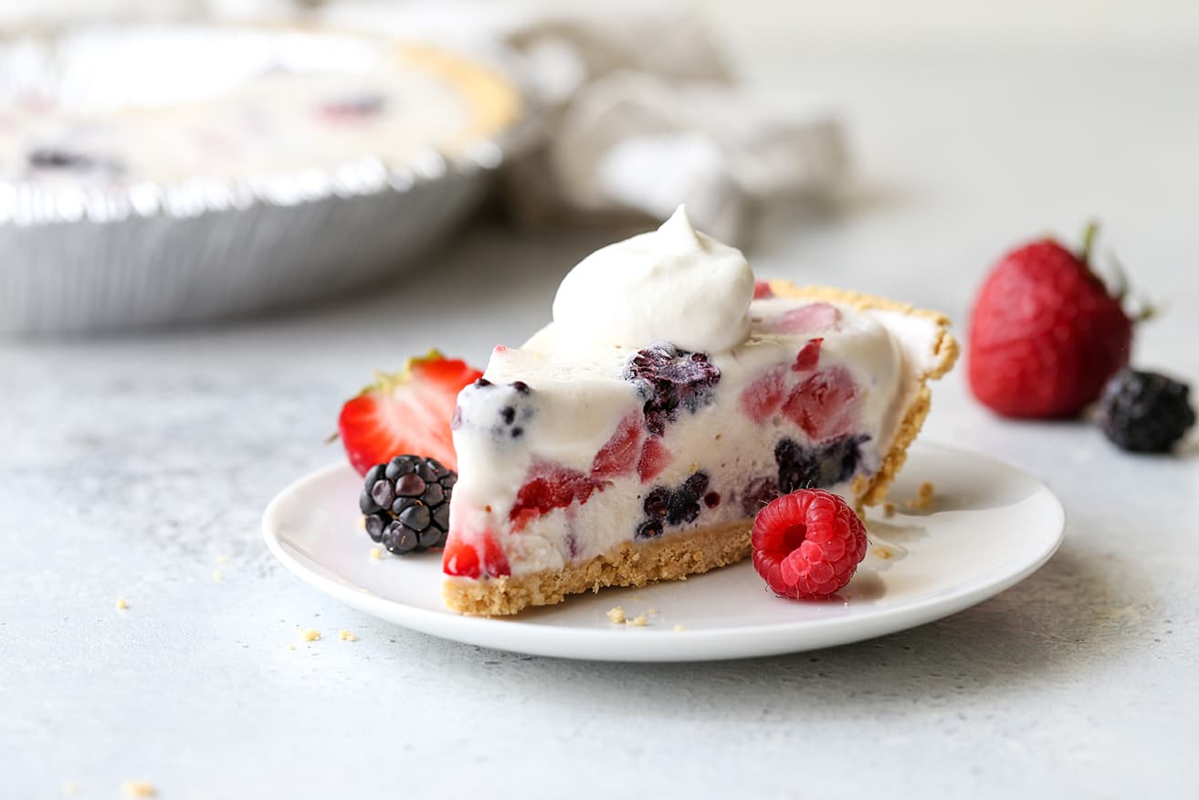 Slice of mixed berry ice cream pie on a plate with a raspberry, strawberry, and blackberry