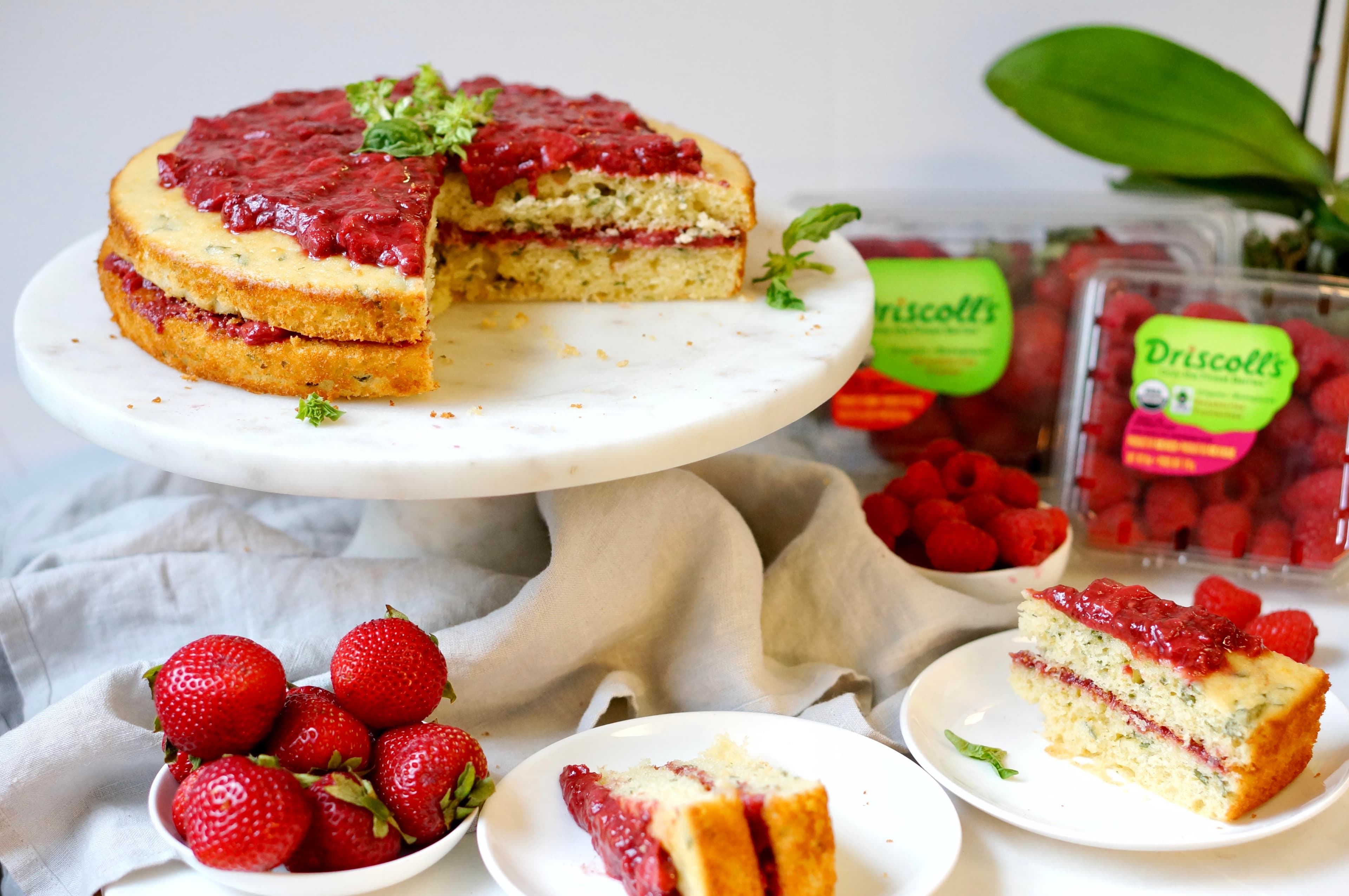 Strawberry raspberry basil cake surround by slices of the cake and fresh strawberries and raspberries