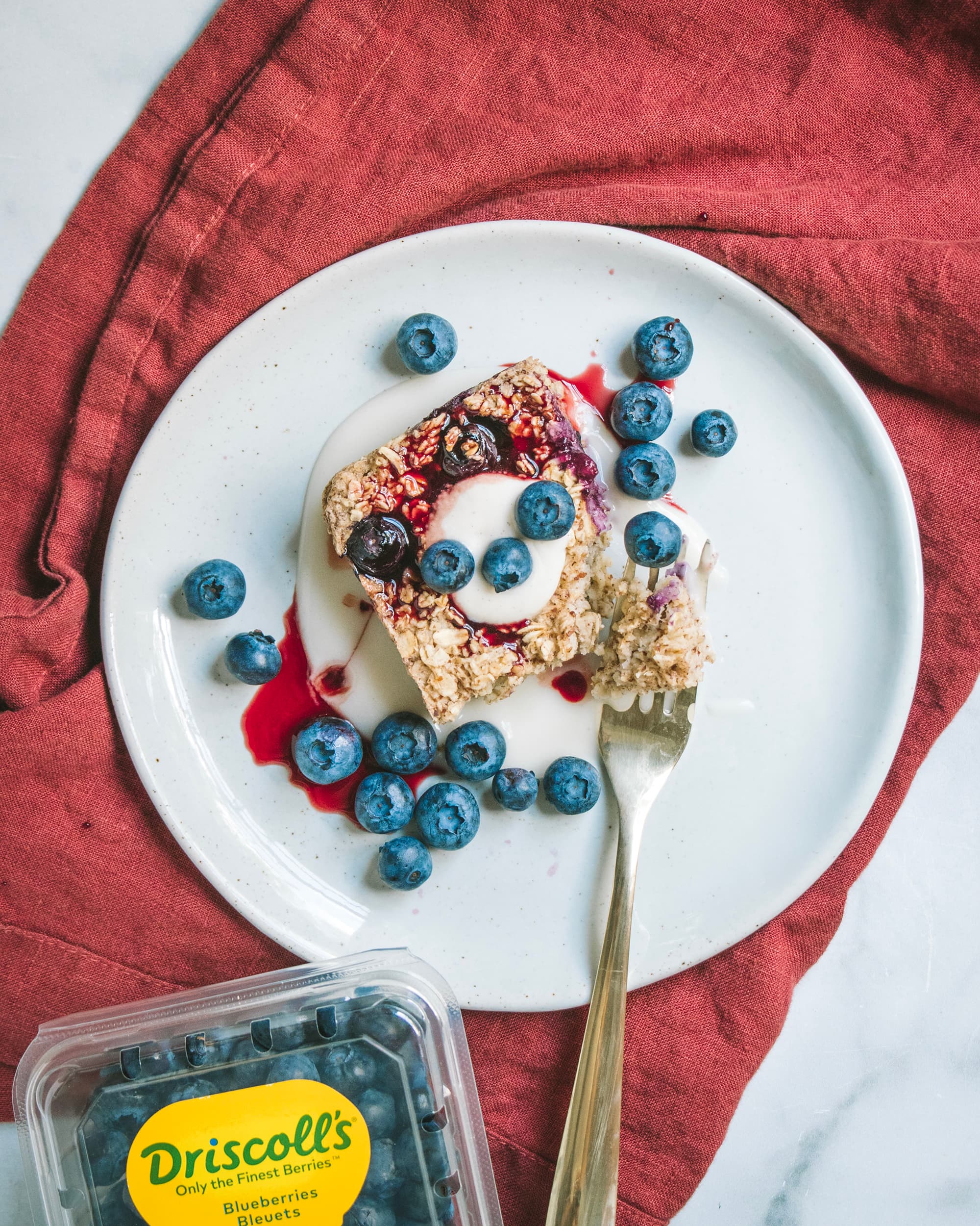 Blueberry baked oatmeal slice sprinkled with blueberries and topped with cream and berry sauce