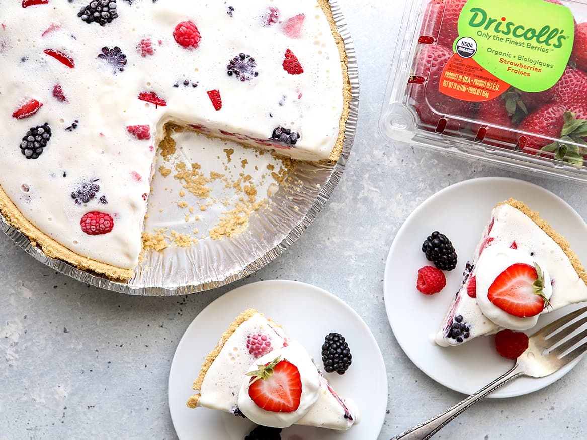 Ice cream cake with mixed berries mixed into the ice cream. 2 slices have been taken out of the pie tin and put onto plates next to a Driscoll's clamshell full of strawberries.