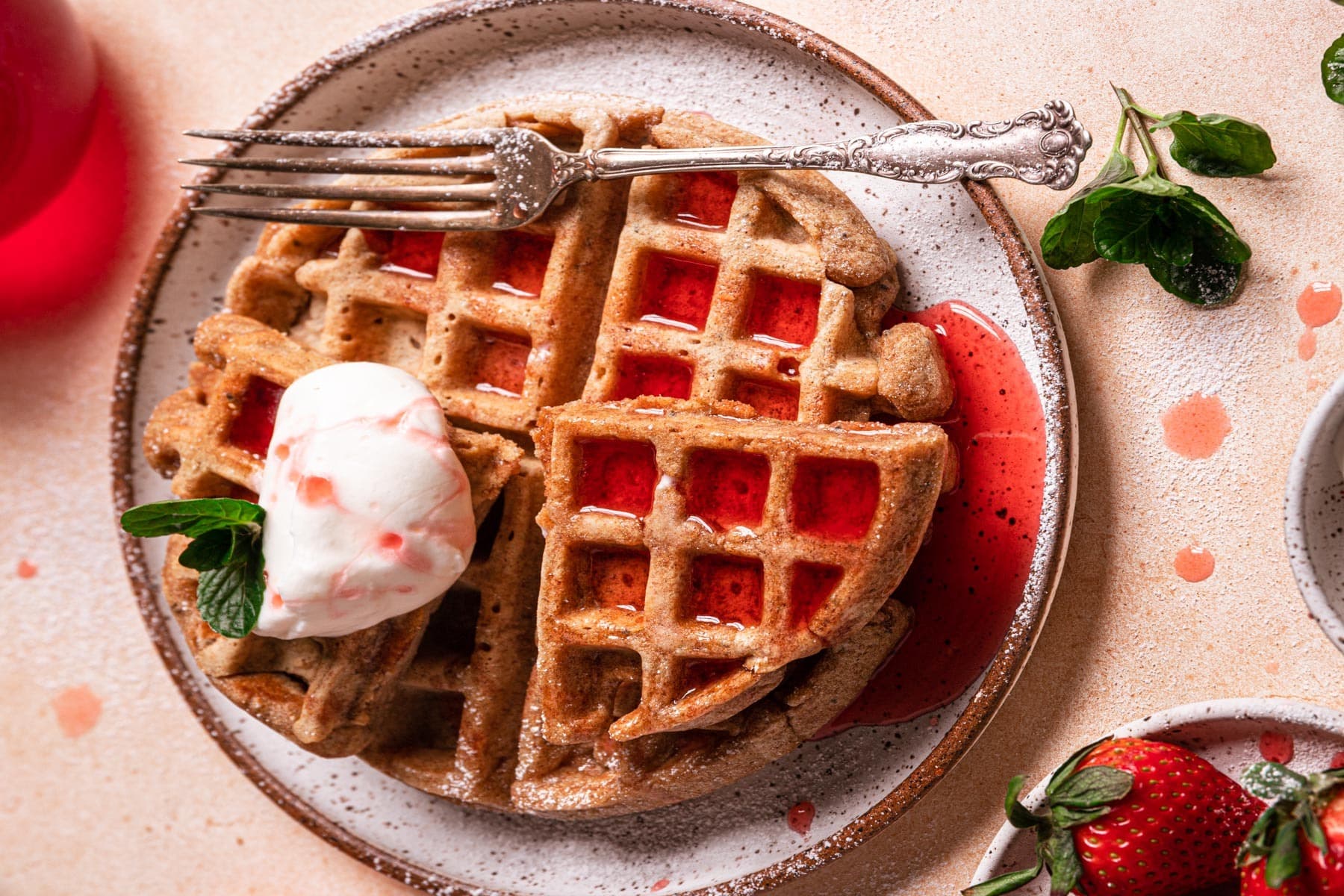 A belgian waffle sitting on a plate, covered in strawberry basil syrup.