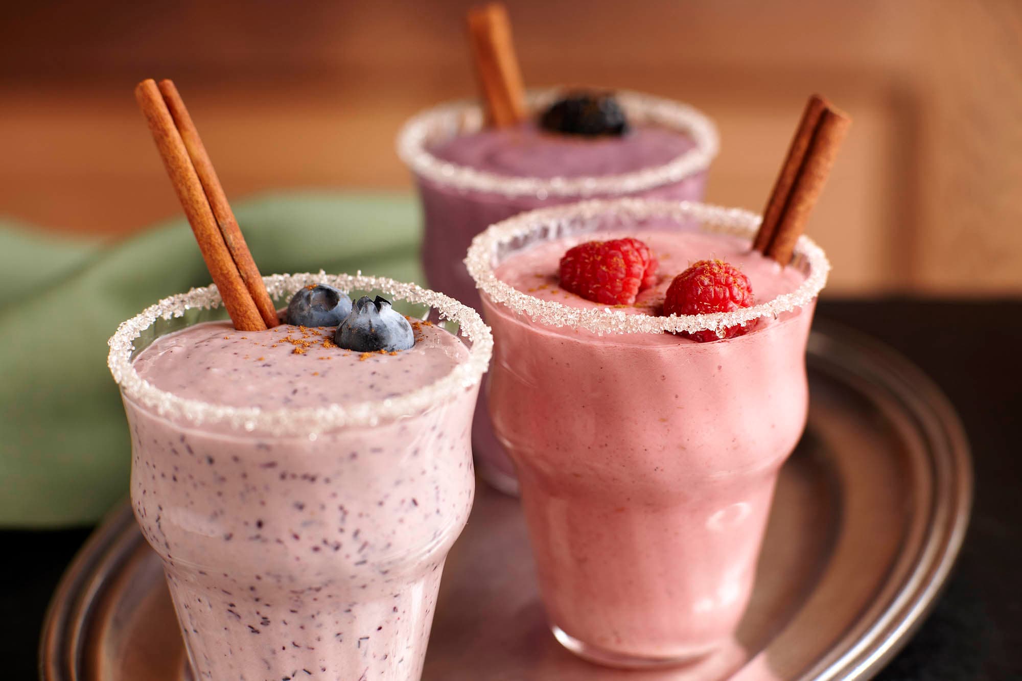 Three glasses of holiday berry nog topped with berries and cinnamon sticks