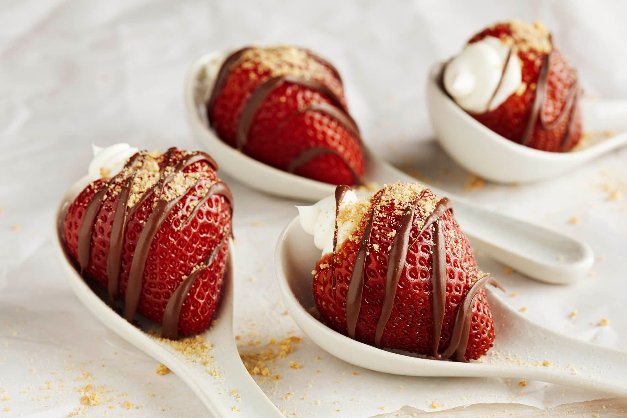 Four spoons holding strawberry cheesecake bites drizzled with chocolate