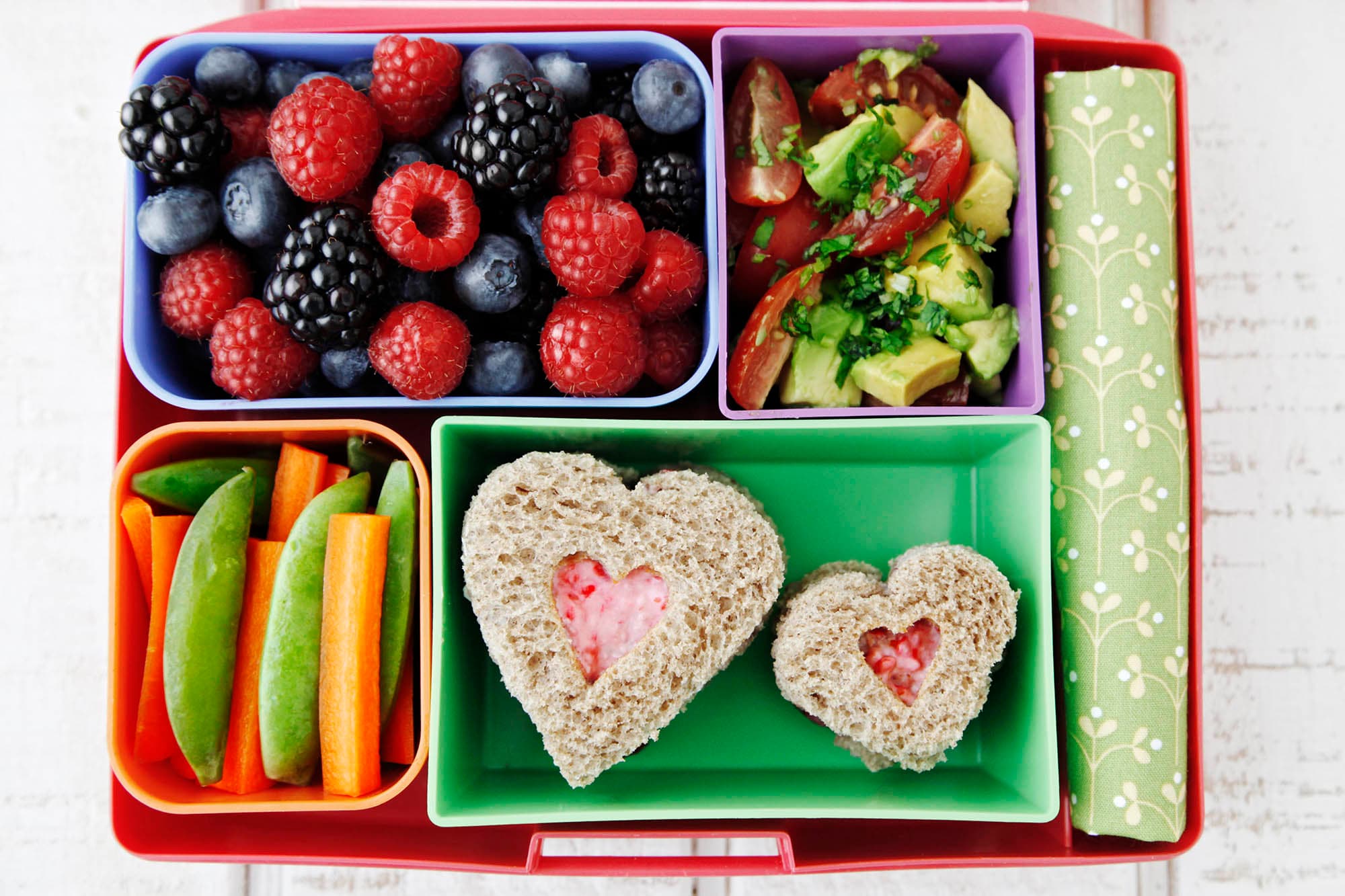 Bento box with heart-shaped raspberry tea sandwiches and a side of berries and vegetables