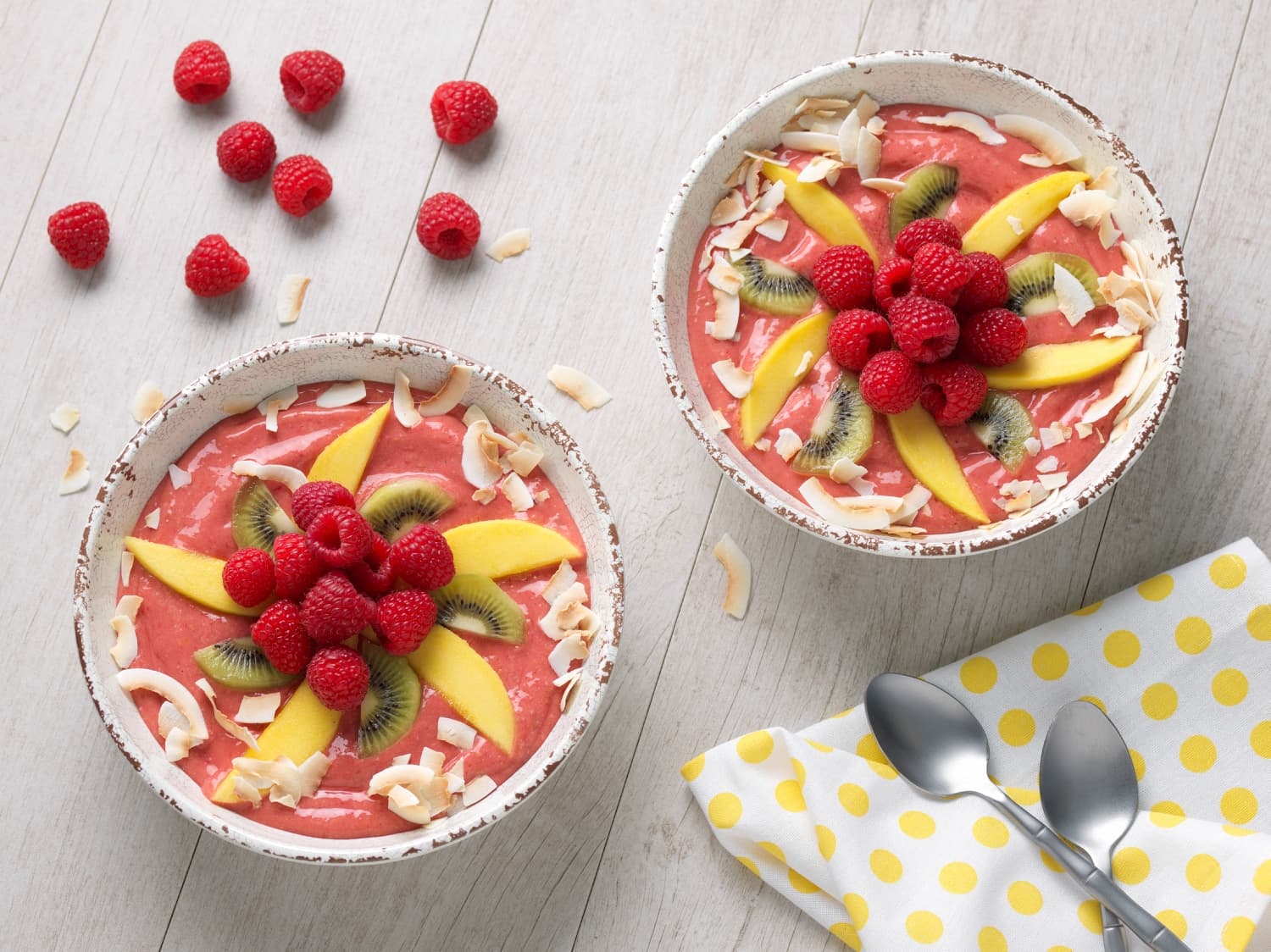Two tropical raspberry smoothie bowls decorated on top with fruit